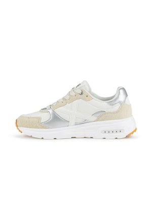 Zapatilla blanca y beige con detalles plateados, diseño con cordones, cuello acolchado y suela blanca gruesa con agarre naranja en la puntera y el talón.