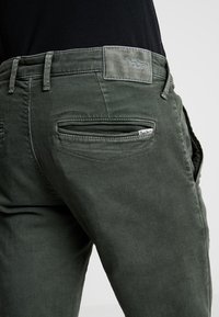 Zelené bavlněné kalhoty slim fit s dvěma zadními kapsami, malou nášivkou s logem a tónovaným šitím pro soudržný design.