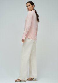 Camisa de manga larga rosa claro con cuello, detalles de botones en los puños, combinada con pantalones anchos blancos de talle alto y tacones beige con tiras.