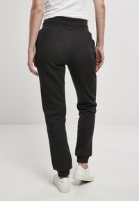 Schwarze Sweatpants aus weichem Stoff mit einem gerippten Bund und Bündchen an den Knöcheln. Minimalistisches Design mit Seitentaschen, von hinten gezeigt.