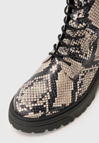 Schnürstiefelette mit einem Schlangenledermuster in Beige und Schwarz, Obermaterial aus strukturiertem Leder und einer stabilen, schwarzen Gummisohle.