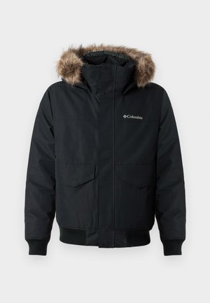 Čierna zateplená bunda s kapucňou vystlanou kožušinou, dvoma prednými vreckami, rebrovanými manžetami a logom na hrudi. Obsahuje zips na uzavretie.