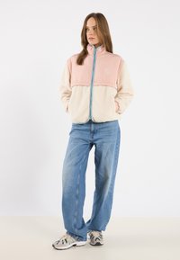 Rövidujjú fleece dzseki rózsaszín felső résszel és krémszínű alsó résszel, cipzárral, magas gallérral és két oldalsó zsebbel.
