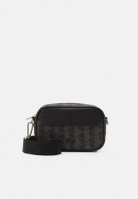 Musta Lacoste olkalaukku, jossa irrotettava leveä hihna ja harmaa geometrinen kuvio etupaneelissa, ylhäällä vetoketjusuljenta.