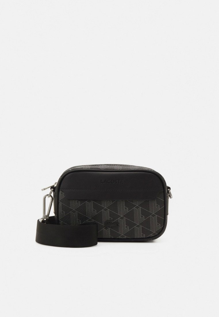 Sac bandoulière noir Lacoste avec sangle large amovible et motif géométrique gris sur le panneau avant, fermeture éclair sur le dessus.