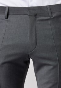 Graue maßgeschneiderte Hose mit flachem Frontschnitt, Gürtelschlaufen und Seitentaschen. Hergestellt aus glattem Stoff mit subtiler Textur und klaren Linien.