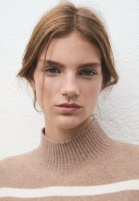 Maglione a collo alto marrone a coste con strisce crema, realizzato in morbida lana. Foto in primo piano che mette in evidenza la texture e i dettagli del colletto.