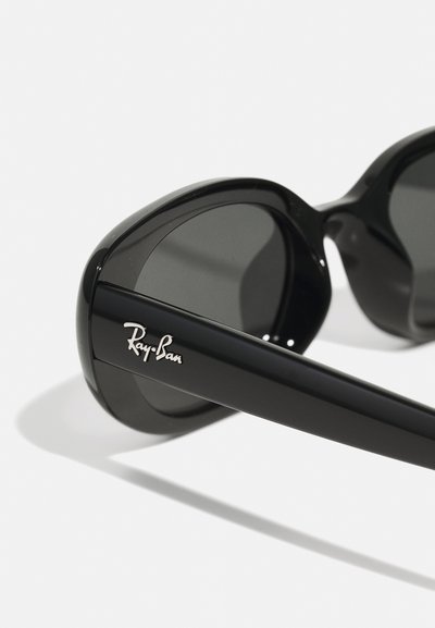 Lunettes de soleil Ray-Ban noires avec une finition brillante, des montures arrondies, des verres foncés et un logo argenté sur la branche.