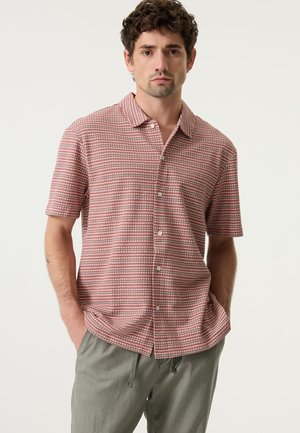 Kurzärmliges Hemd mit Knöpfen in rot-weißem Karomuster, mit Kragen und leichtem Stoff. Kombiniert mit grauen Shorts.