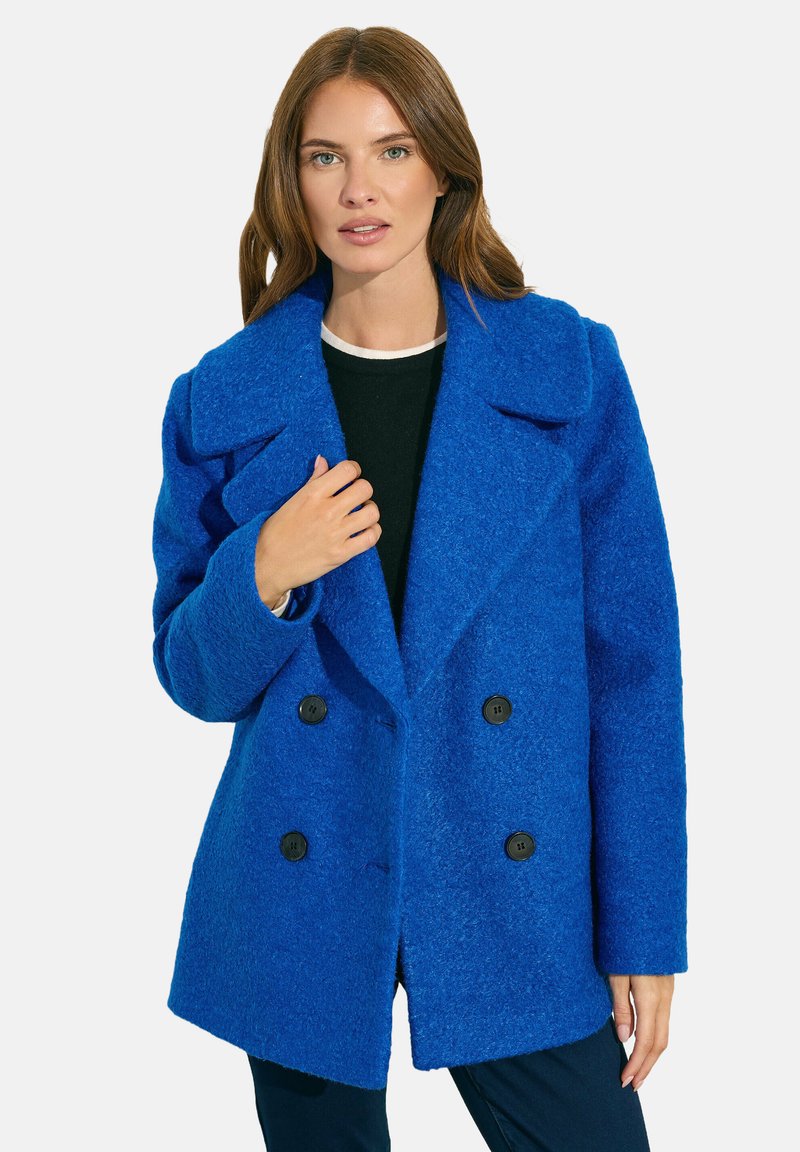 Sininen kaksirivinen villatakki, jossa on suuret kaulukset, teksturoitu pinta, neljä nappia ja rento istuvuus. Päällä musta paita.