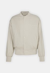 Veste bomber beige en tissu doux, dotée d'une fermeture à bouton-pression, de poignets côtelés et d'un détail brodé "New York City 1990".