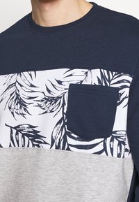 Sudadera en navy y gris con un panel de estampado floral, un bolsillo en el pecho y un cuello redondo. Diseño minimalista con estilo casual.