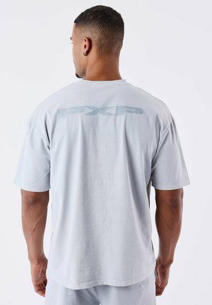 Camiseta de manga corta gris claro con un sutil logo "PXP" en la parte posterior. Fabricada en una tela suave, con un corte holgado y una textura suave.