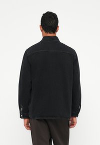 Giubbotto in denim nero con vestibilità rilassata, maniche lunghe e dettagli con bottoni ai polsini. Tessuto morbido con accenti di cucitura minimi.