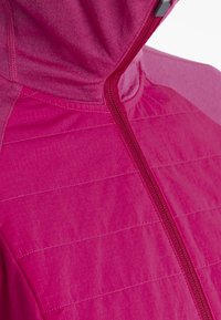 Veste à capuche rose vif avec une fermeture éclair frontale et des motifs de couture horizontale discrets sur le tissu.
