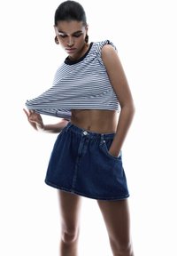 Randig crop top i vitt och marinblått, kombinerad med en högmidjad denimkjol. Kjolen har synliga fickor och en knapppdetail fram.