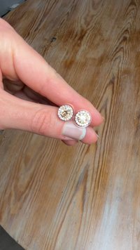 Kerek fülbevalók, középen bézs színű kővel, amelyet áttetsző kövek gyűrűje vesz körül, ezüstszínű fémből, kézben tartva.