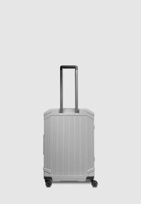 Maleta rígida gris con ranuras verticales, asa negra extensible, cuatro ruedas y esquinas redondeadas para estabilidad y fácil movilidad.