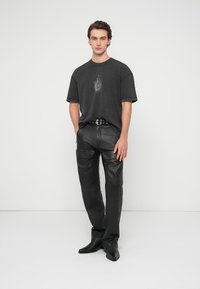 Mørkegrå, oversized bomulls-T-skjorte med et subtilt grafisk trykk, kombinert med svarte skinnbukser med sidelommer og et svart belte.