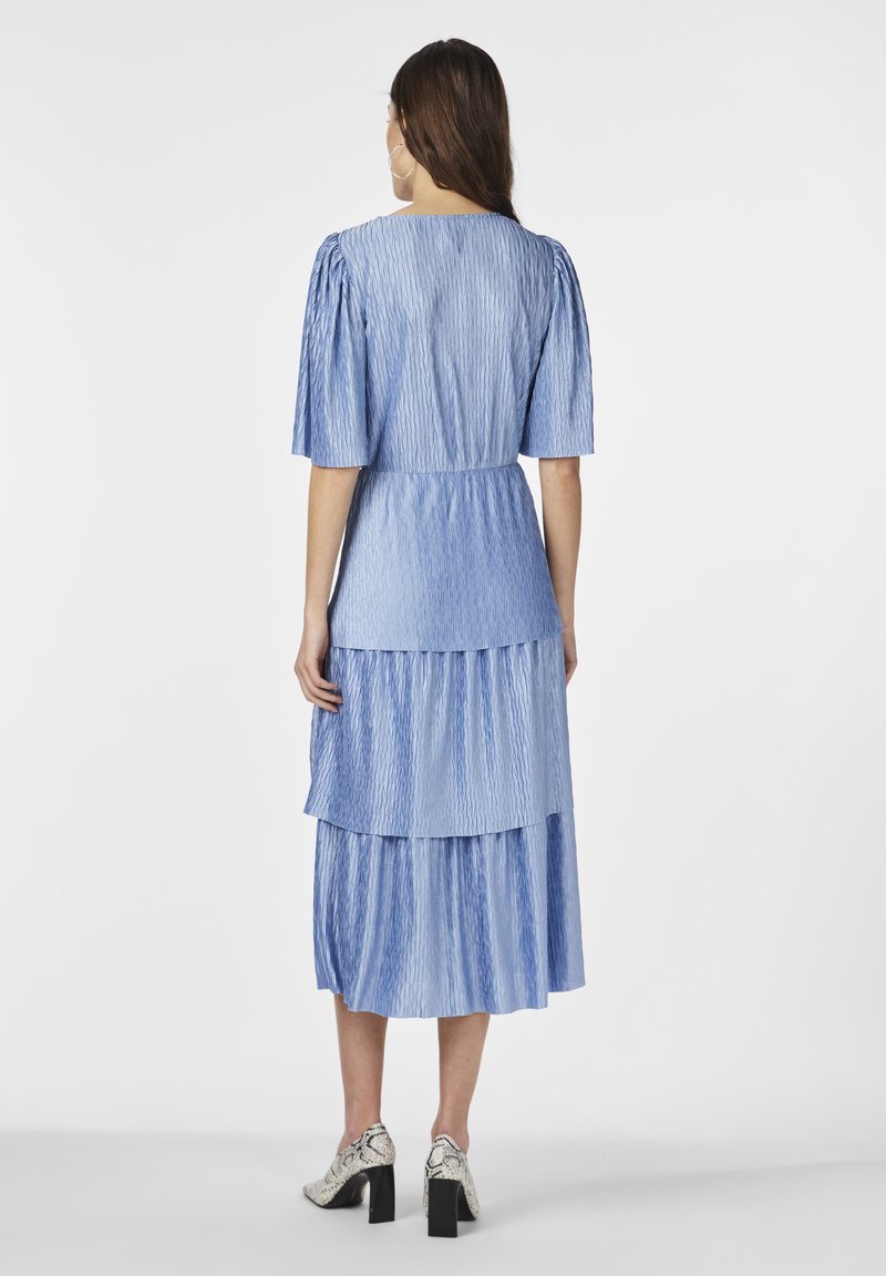 Niebieska sukienka warstwowa z bufkami, teksturowany materiał i dopasowana talia. Posiada falbany i długość do kolan, w połączeniu z teksturowanymi obcasami w klocku.