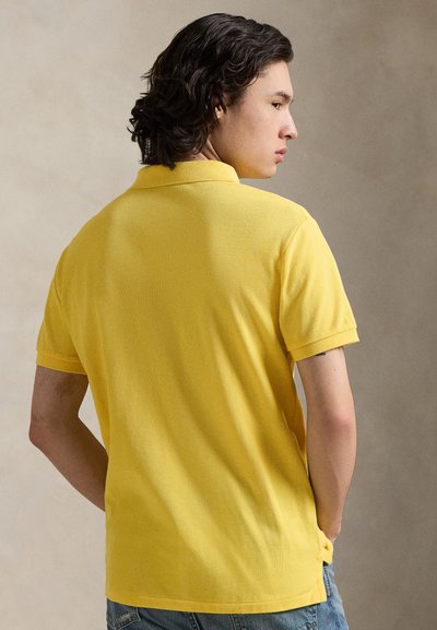 Κίτρινο πόλο μπλουζάκι με υφή, κοντά μανίκια και γιακά. Διαθέτει πλαϊνές σχισμές στο κάτω μέρος και άνετη εφαρμογή.