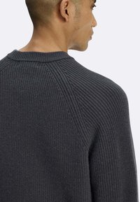 Maglione grigio lavorato a maglia con collo tondo, maniche raglan e dettagli a coste lungo il colletto e le spalle.