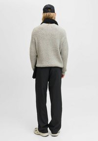 Suéter de punto texturizado gris con mangas largas; pantalones negros a rayas; usando una gorra negra. Ajuste relajado en general, diseño minimalista.
