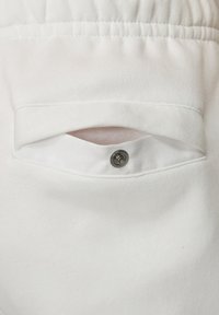 White fabric pocket with a snap closure, featuring a soft texture and elastic waistband above. The design is simple and functional.