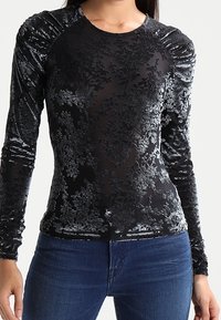Svart långärmad skjorta i sammet med blommönster, med rynkade axeldetaljer och en figurnära silhuett.