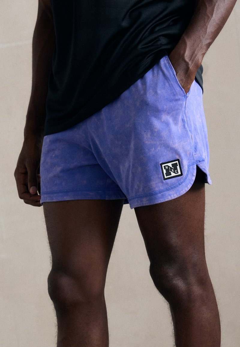 Lila Shorts aus weichem Stoff, mit einem verblassten Design, Seitentaschen und einem schwarzen Nike-Logopatch am Saum.