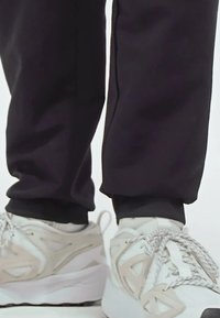 White sneakers with textured accents and gray detailing, paired with black tapered pants ending at the ankle.