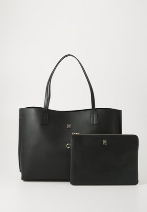 Sac tote en cuir noir avec doubles poignées et pochette zippée. Texture lisse, accents en métal doré, logo embossé sur les deux pièces.