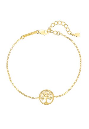 Nahaufnahme eines Handgelenks mit einem zarten goldenen Armband mit einem Baum-Anhänger, Hand nahe am Gesicht erhoben, sichtbares dunkles Haar und braunes Oberteil.