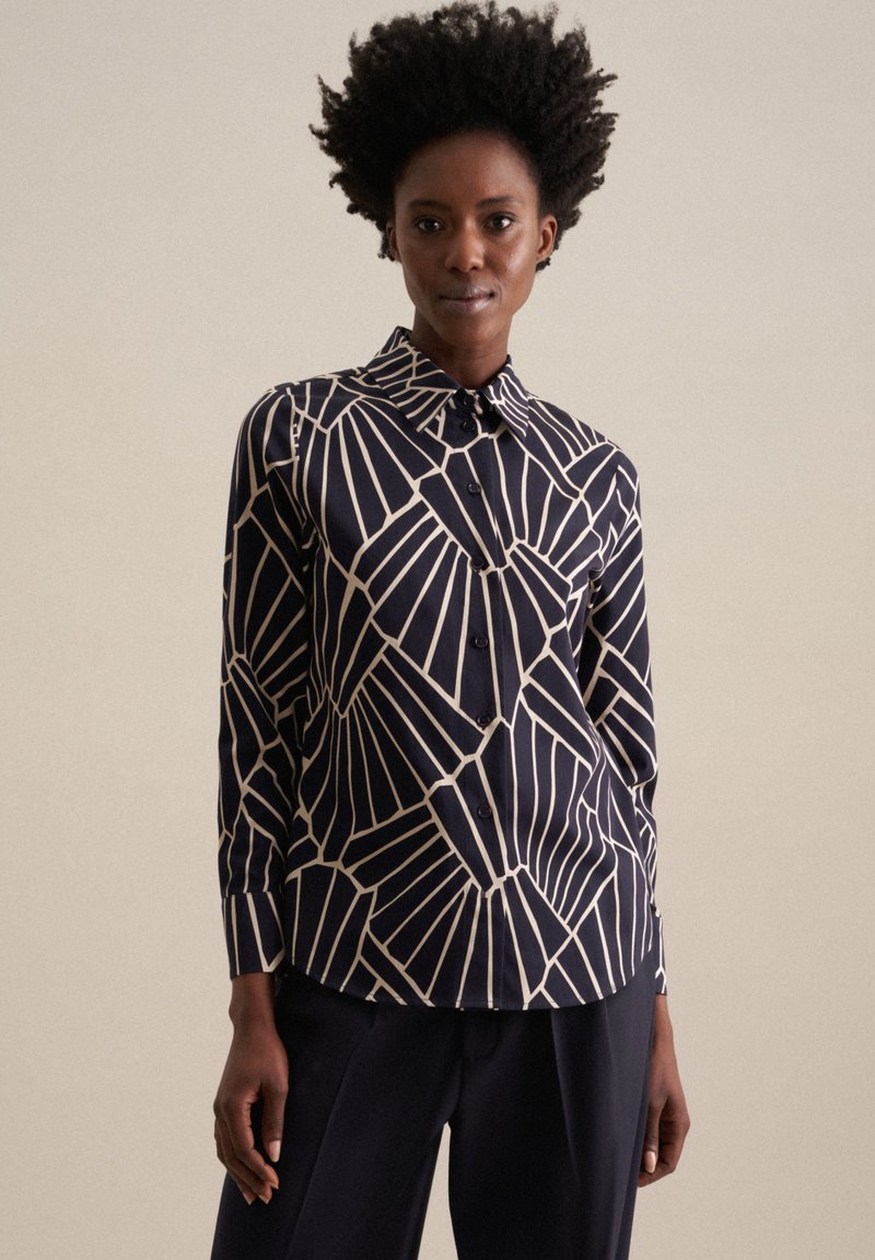 Chemise bleu marine à boutons avec un motif géométrique blanc, dotée d'un col classique, de manches longues et d'un ourlet légèrement incurvé. Texture lisse.