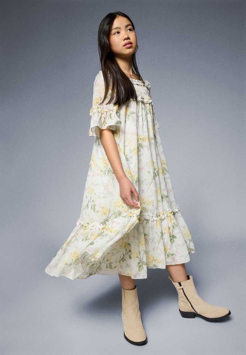 Gėlėta suknelė šviesiomis pastelinėmis spalvomis su ruffles ir kelių lygių apatine dalimi. Suderinta su rusvomis aulinėmis batais su šoniniu užtrauktuku.