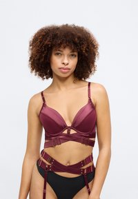Sostén de satén color malva con copas profundas y tirantes ajustables, que presenta herrajes decorativos en dorado y un diseño estilo arnés en la cintura.