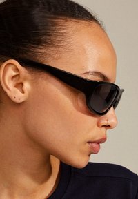 Black sunglasses with a thick frame, polarized lenses, and angular design. Smooth texture and minimal accents, viewed from the side.