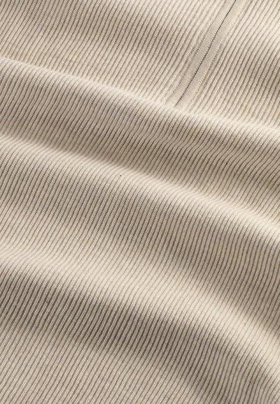 Primo piano di tessuto beige a coste con cuciture dettagliate e morbide pieghe che creano texture e ombre.