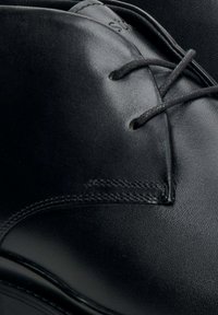 Czarne skórzane buty o gładkiej fakturze, zaokrąglonym nosku, sznurowanym fasonie i subtelnych detalach wzdłuż krawędzi.