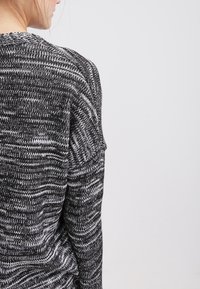 Svart och vit mönstrad stickad tröja med en texturerad yta, med rund halsringning och raglanärmar, sedd från baksidan.