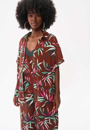 Bruine bloemen button-up jurk met korte mouwen, versierd met groene en roze bladeren, gelaagd over een zwarte kant camisole.
