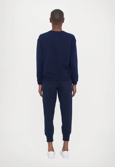 Marineblå hettegenser og joggebukser laget av mykt stoff, med ribbestrikkede mansjetter og en klassisk crew neck-design, sammen med hvite sneakers.