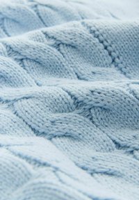 Světlomodrá pletená látka s texturovaným vzorem se zapletenými kabely, vytvářející hloubku díky měkké, nadýchané přízi.