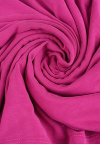 Fuchsia bomullstyg, vridet i veck, som visar en slät textur och jämnt stickat mönster, med synlig söm längs kanterna.