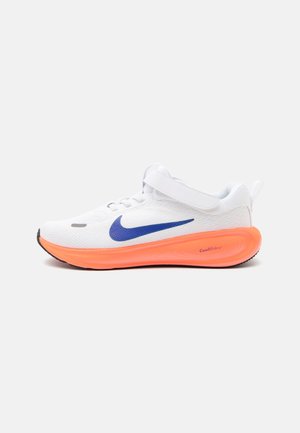 Fehér sportcipő kék Nike logóval, narancssárga talppal, fekete orr-résszel és tépőzáras pánttal a fűzők felett, világos háttéren.