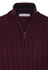 Jersey de punto burdeos con un diseño de cable, cuello de media cremallera y ribete de cuello acanalado con rayas oscuras. Etiqueta de marca visible en el interior.