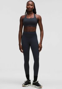 Mörkgrå sport-bh och högmidjade leggings gjorda av elastiskt material. Bärs med svarta träningsskor med en ljus sula.