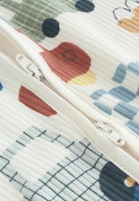 Baumwollstoff mit gerippter Struktur, versehen mit einem bunten abstrakten Druck in den Farbtönen Rot, Grün, Blau und Gelb sowie einem weißen Reißverschluss.