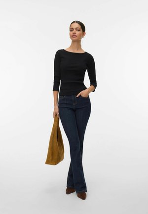 Haut noir côtelé à manches trois-quarts, jeans évasés foncés, et sac à main en daim beige, assortis à des chaussures marron à bouts pointus.