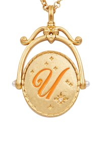 Zelta kulons ar ovālu formu, kurā ir oranžs "U" kursīvā, ko ieskauj zvaigznes un mazas pērles katrā pusē.